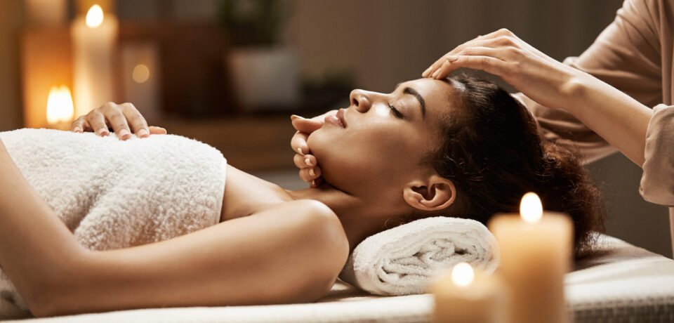 Attractive african girl enjoying face massage in spa salon. Closed eyes.
