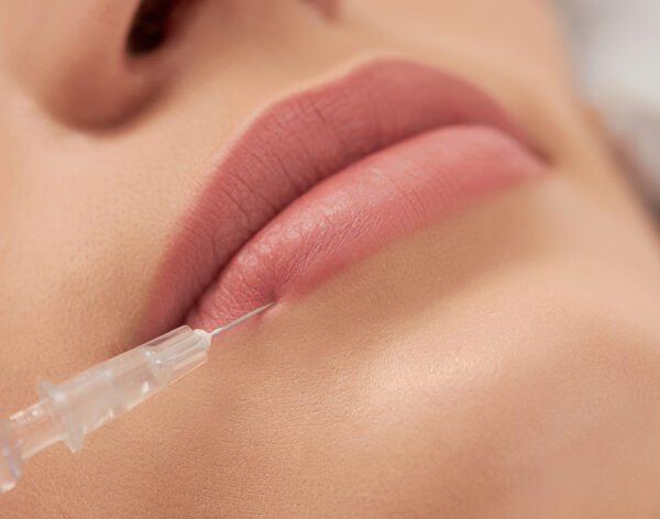 Close up of beautician in rubber gloves doing procedure lip augmentation for young beautiful woman in professional salon. Concept of beauty procedure with good mood.